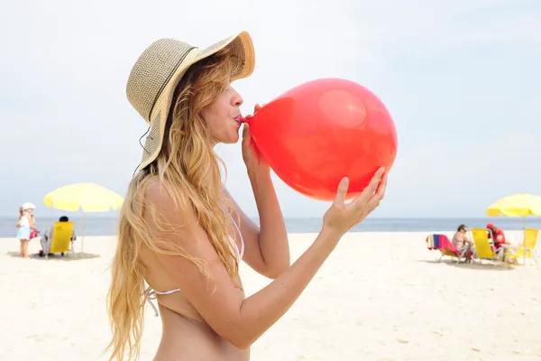 Mulher inflando um balão vermelho na praia — Fotografia de Stock