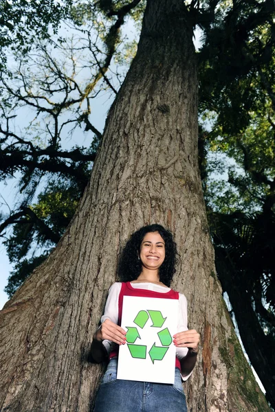 Riciclaggio: donna davanti a un albero con un cartello di riciclo — Foto Stock