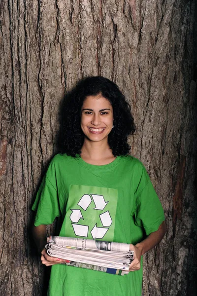 Жінка зі знаком переробки на сорочці, що тримає газети — стокове фото