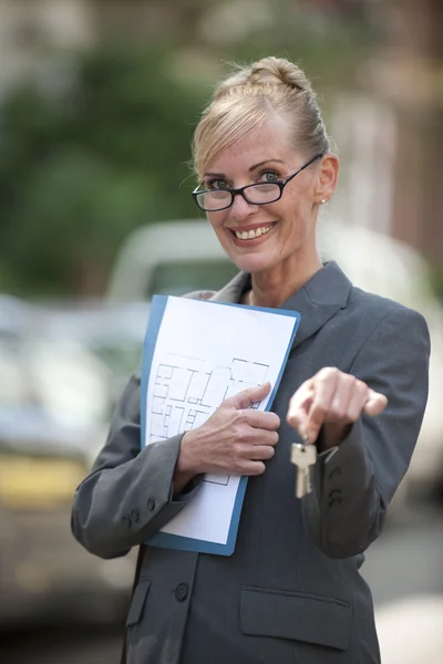 Agente inmobiliario femenino sosteniendo llave de la casa — Foto de Stock