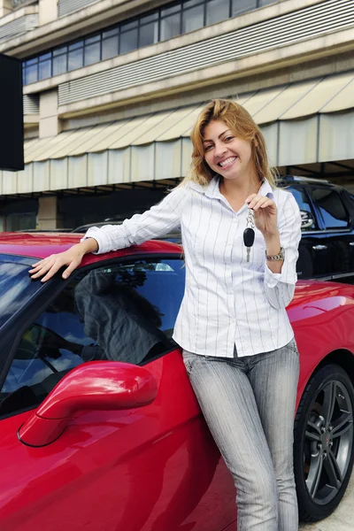 Женщина показывает ключ от нового красного спортивного автомобиля — стоковое фото