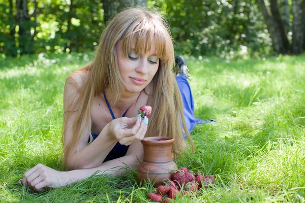 A mulher em uma grama e um morango com o leite — Fotografia de Stock