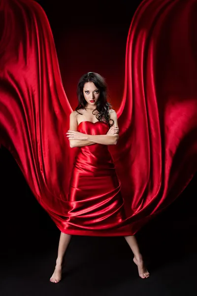 Mujer misteriosa en vestido de seda ondulante rojo sobre fondo negro —  Fotos de Stock