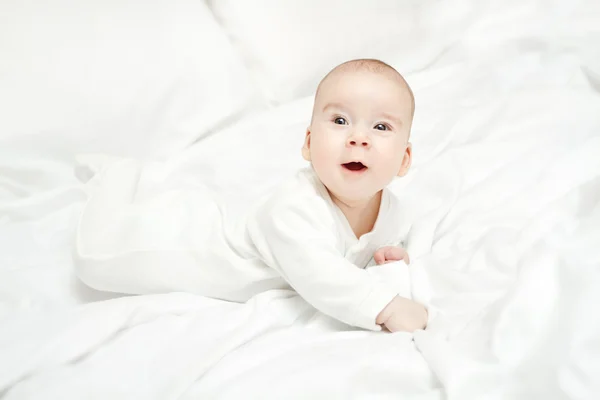 Glad aktiva barnet ligger på mage över vit säng. tre månaders — Stockfoto