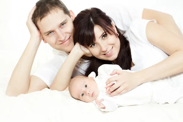 Happy family, parents embracing newborn baby lying down over whi — 图库照片