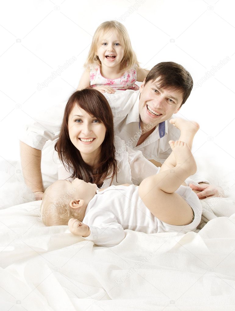 Happy family: parents playing with two kids in bed. Looking at c