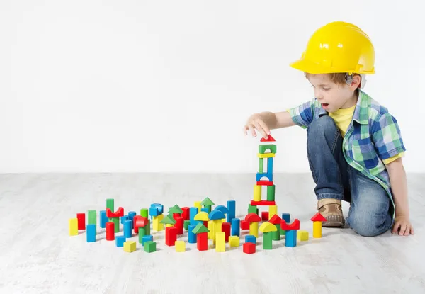 Crianças brincam quarto, criança em chapéu duro jogando blocos de construção brinquedos — Fotografia de Stock