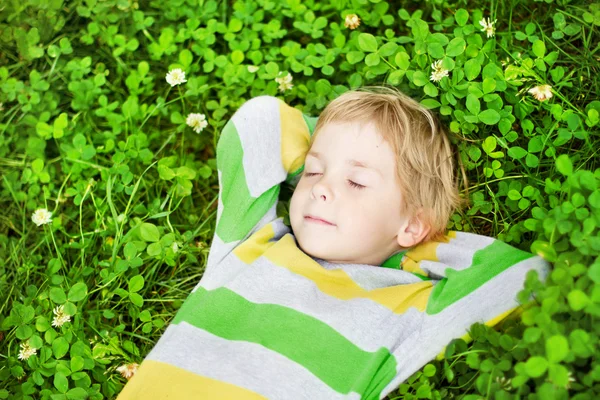 Küçük çocuk dışarıda çimenlerin üzerinde uyku ellerini başının arkasında. yüksek — Stok fotoğraf