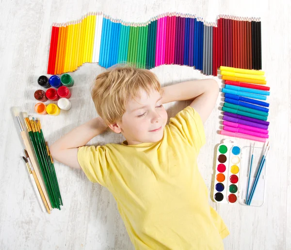 Child dreaming lying next to pencils, brushes and paints. Creat — Stock Photo, Image