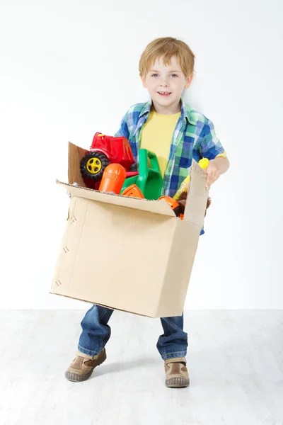 Child holding cardboard box packed with toys. Moving and growing — Stock Photo, Image