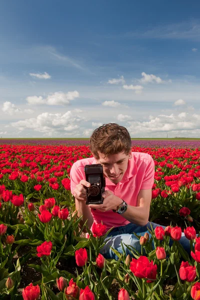 Jovem com câmera de foto antiga no campo com tulipas — Fotografia de Stock