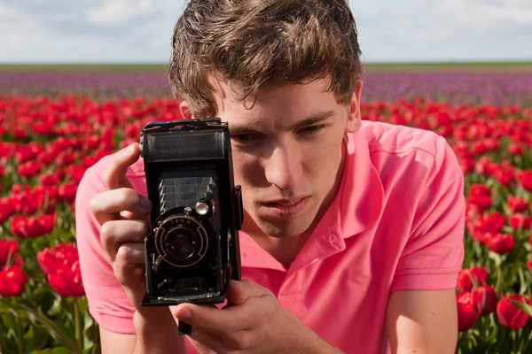 Yong hombre con cámara de fotos de edad en el campo con tulipanes —  Fotos de Stock