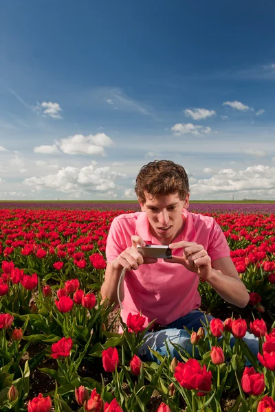 Yong homem com câmera de foto velha no campo com tulipas — Fotografia de Stock