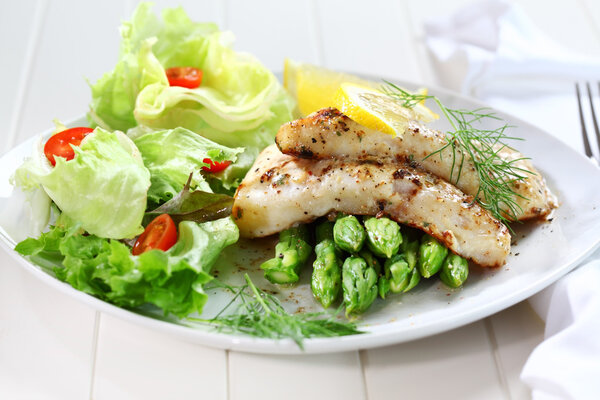 Fried fish on green asparagus with salad