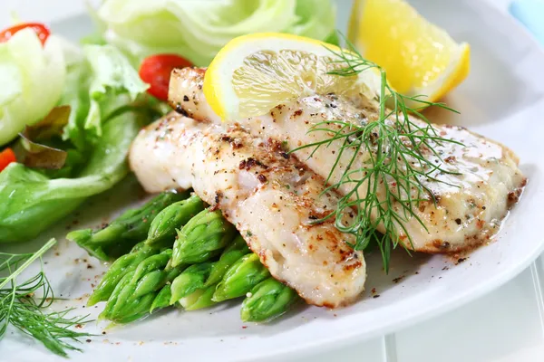Gebratener Fisch auf grünem Spargel mit Salat lizenzfreie Stockfotos