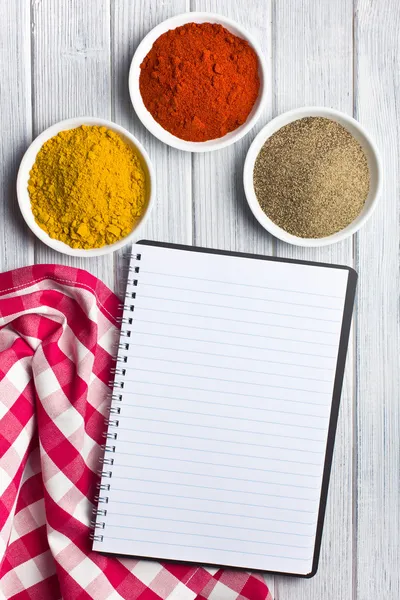 Verschillende gekleurde kruiden met lege receptenboek — Stockfoto