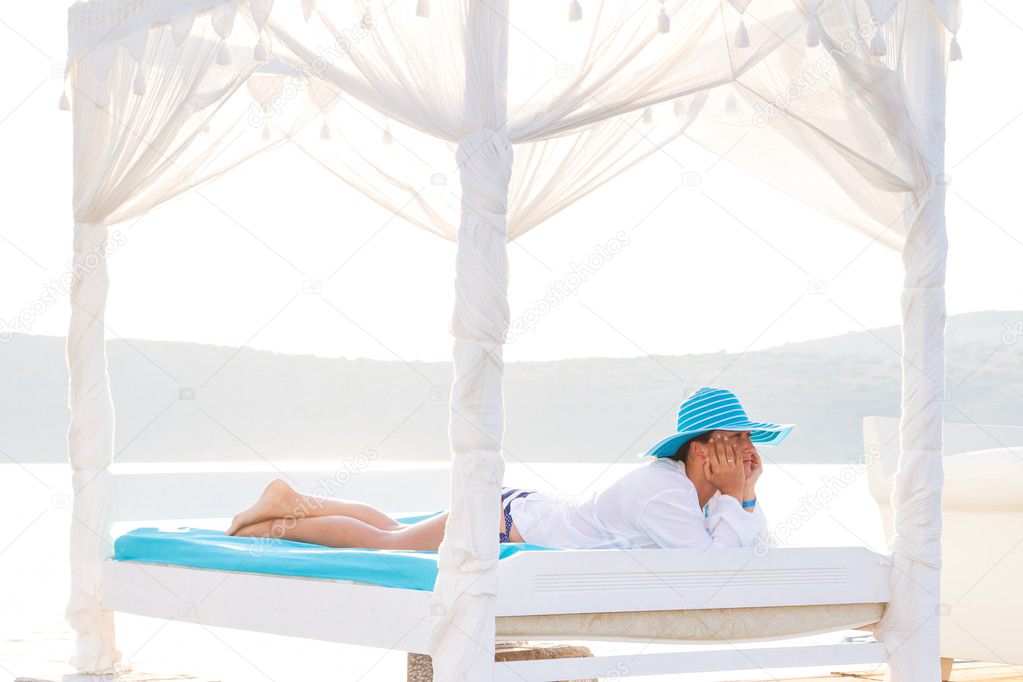 Woman in hat relaxing on luxury white bed