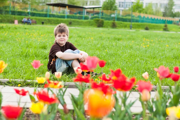 The boy sitting next to the flowerbed with tulips — Stock Photo, Image
