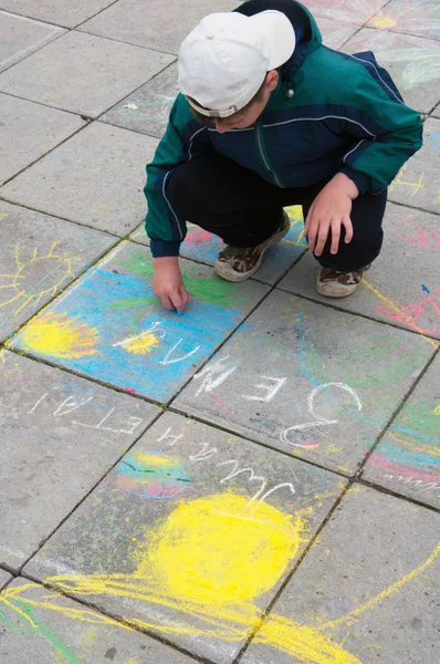 Een jongen schildert krijt op de stoep — Stockfoto
