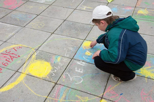 Мальчик рисует мелом на тротуаре — стоковое фото