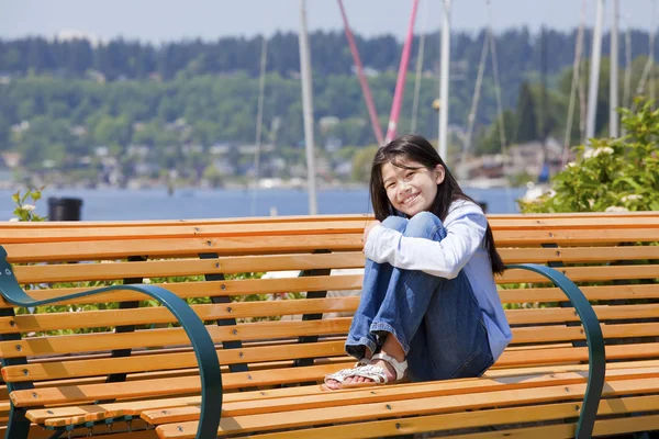 十岁女孩享受阳光在湖边的长椅上， — 图库照片