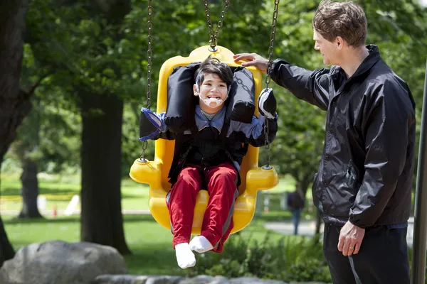 Pai empurrando menino deficiente em necessidades especiais swing — Fotografia de Stock