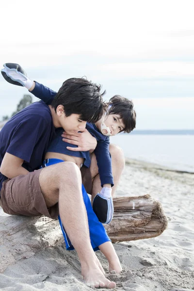 Старший брат держит мальчика-инвалида на пляже — стоковое фото