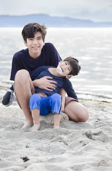 Старший брат держит мальчика-инвалида на пляже — стоковое фото