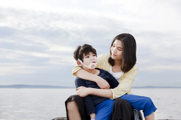 Teenage sister holding her disabled brother on the beach — Stock Photo, Image