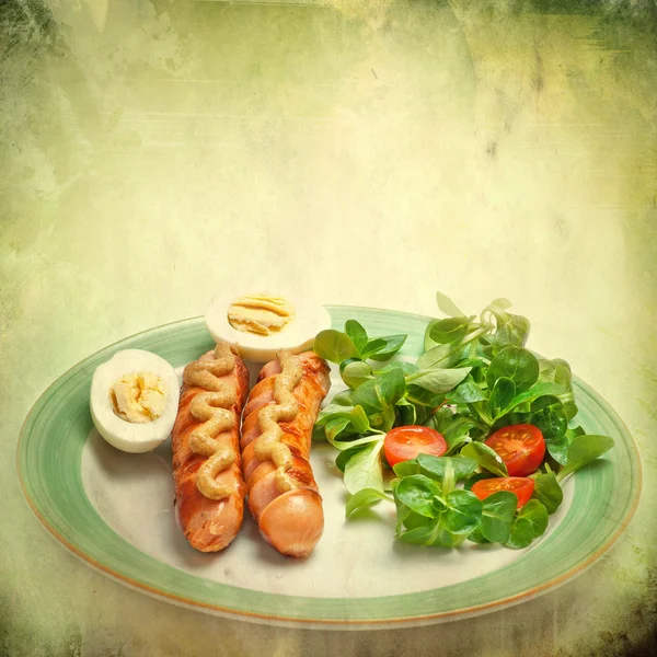 Sausages on the grill with mustard, egg, salad and tomatoes on grunge background — Stock Photo, Image