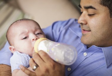 Happy Hispanic Father Bottle Feeding His Son clipart