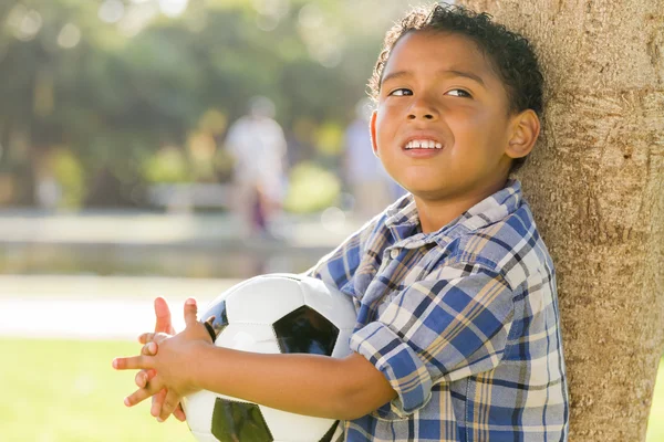 Un garçon de race mixte tenant un ballon de football dans le parc contre un arbre — Photo