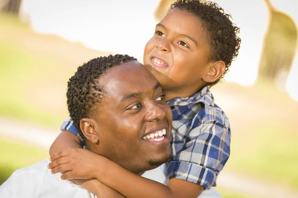 Mieszanej rasy ojciec i syn gra piggyback w parku — Zdjęcie stockowe