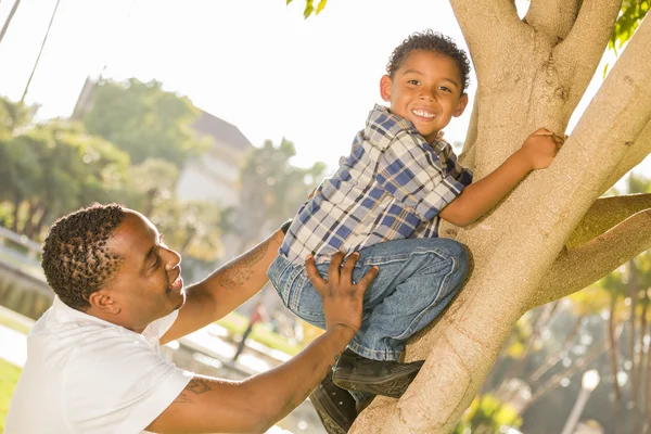 Szczęśliwy mieszanej rasy ojciec pomoc syna wspiąć się na drzewo — Zdjęcie stockowe