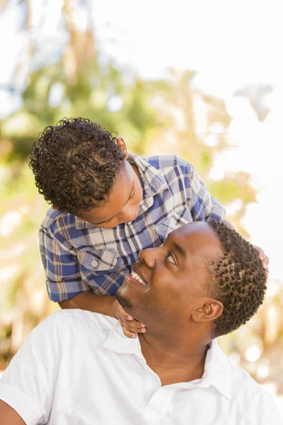 Mieszanej rasy ojciec i syn gra piggyback w parku — Zdjęcie stockowe