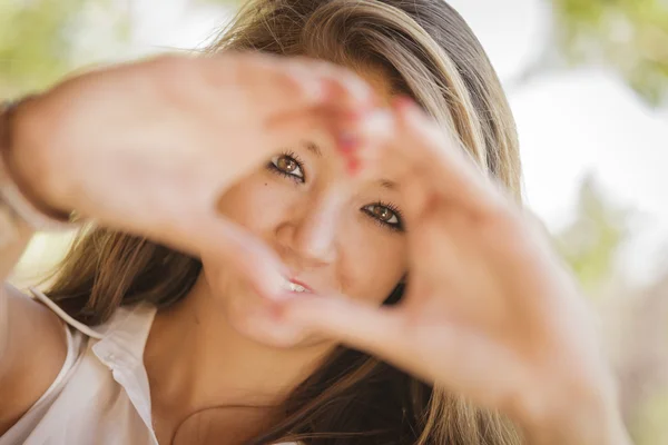 Atractivo retrato de niña de raza mixta sonriente con signo de mano de corazón —  Fotos de Stock