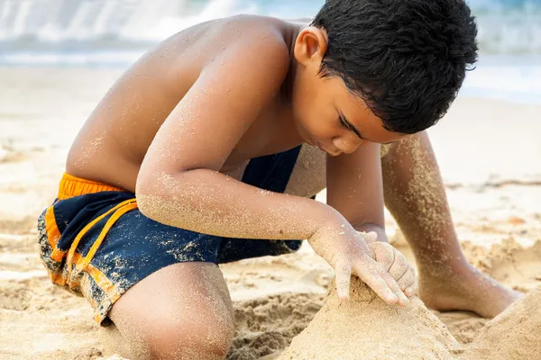 Menino hispânico construindo um castelo de areia — Fotografia de Stock