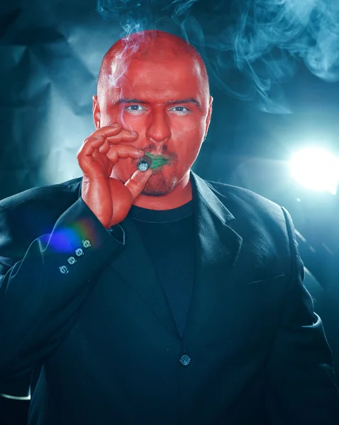 Tajemný muž s červenou tváří kouření doutníku. — Stock fotografie
