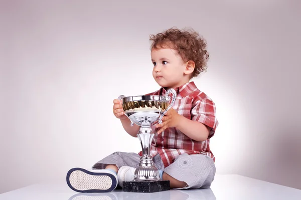 Menino pequeno sentado e segurando um troféu — Fotografia de Stock