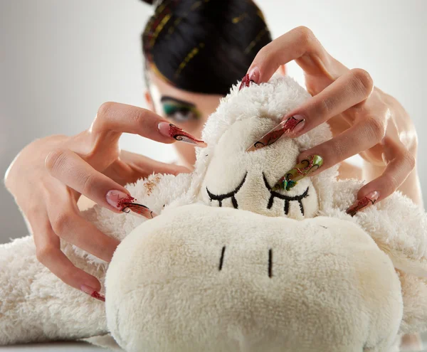 Young woman sticking her nails in her lamb toy — Stock Photo, Image