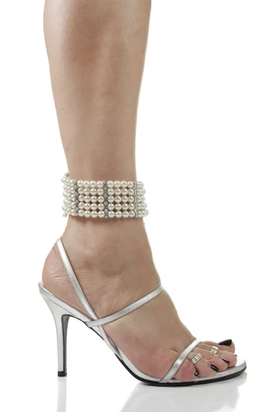 Pieds de femme portant des chaussures à talons argentés et des perles sur fond blanc — Photo