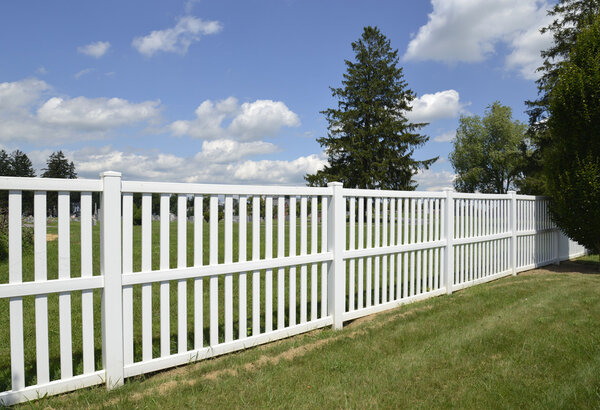 Белый виниловый забор на зеленой лужайке
