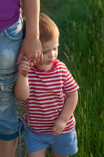 Cute little boy holding hand of his mother while walking on the meadow — Stock Photo, Image