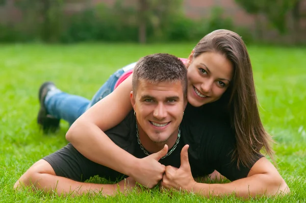 对年轻夫妇在爱躺在草地上和出现的拇指 — 图库照片