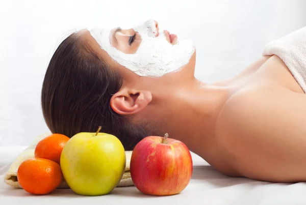 Beautiful young woman lying on massage table with natural facial mask on her face — Stock Photo, Image