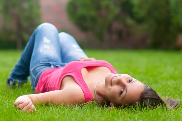 Vacker leende flicka liggande i gräset på lugna vårdag — Stockfoto