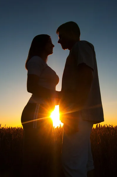 Silhuetas de jovem casal ao pôr do sol no belo dia de verão — Fotografia de Stock
