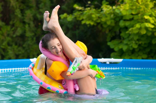 Two teenage girls having fun in the home swimming pool with their childhood toys — Stock Photo, Image