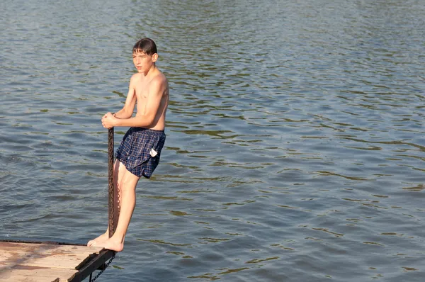 十几岁的男孩站在边缘的木码头上在阳光灿烂的夏天一天 — 图库照片