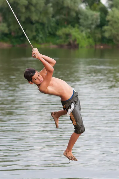 Nastoletni chłopiec skoki do rzeki od wychylenia liny — Zdjęcie stockowe